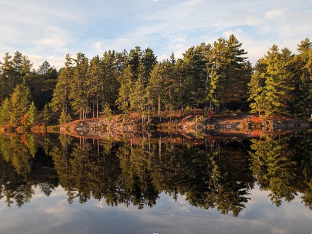 Calm backcountry lake reflecting fall pines at sunset, the secluded largemouth bass fishery overlooking Lake Nipissing