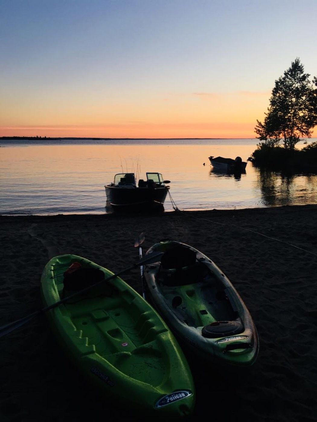 Outdoor gear including kayaks and a fishing boat on the beach
