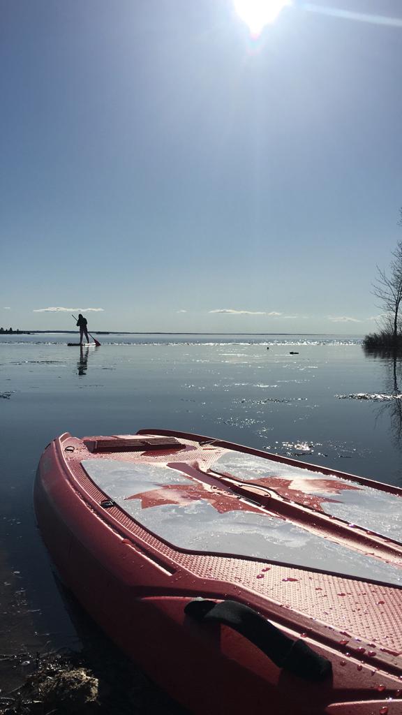 Stand-up paddleboard rental on calm Lake Nipissing water with person paddleboarding in the distance
